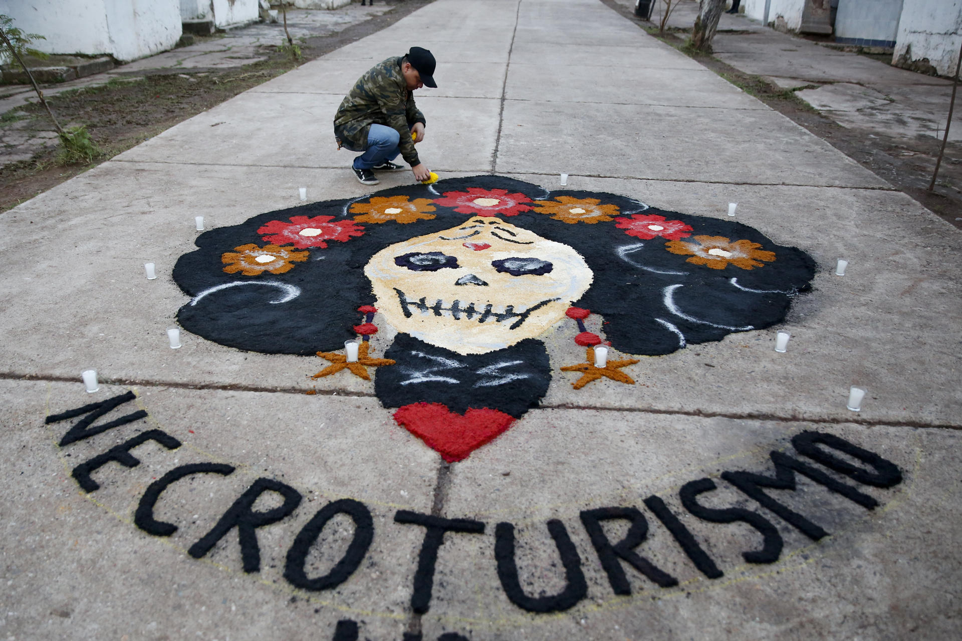Un hombre coloca una flor a una alfombra de aserrín hecha en el Cementerio General, en el marco de Día de Muertos, este sábado de la ciudad de Comayagüela (Honduras). EFE/Gustavo Amador