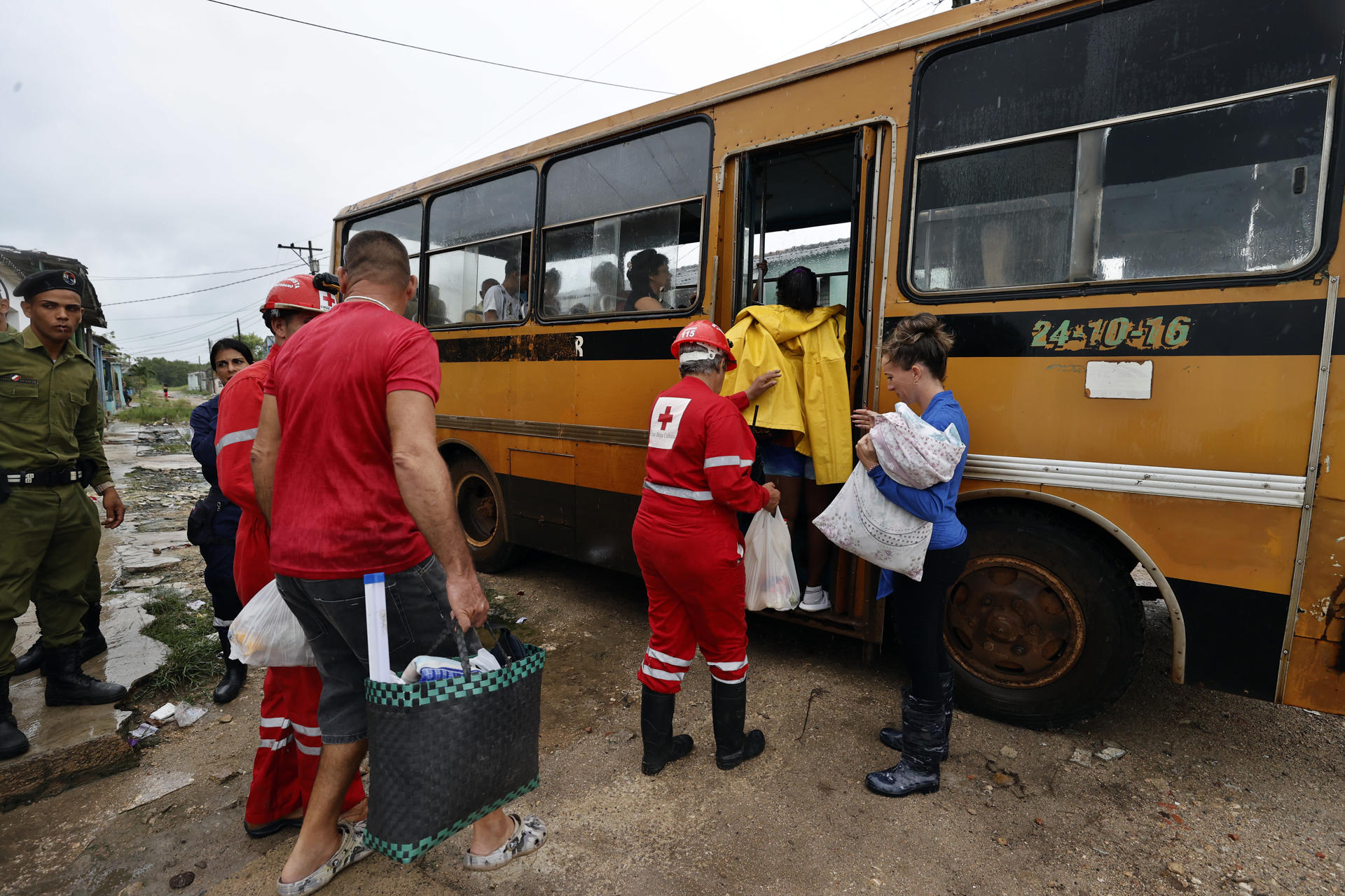 Integrantes de la Cruz Roja cubana ayudan a unas personas a subir a un autobús durante una evacuación ante la llegada del huracán Rafael, este miércoles en Surgidero de Batabanó, un puerto pesquero en la provincia occidental de Mayabeque, a unos 50 kilómetros al sur de La Habana (Cuba). EFE/ Ernesto Mastrascusa
