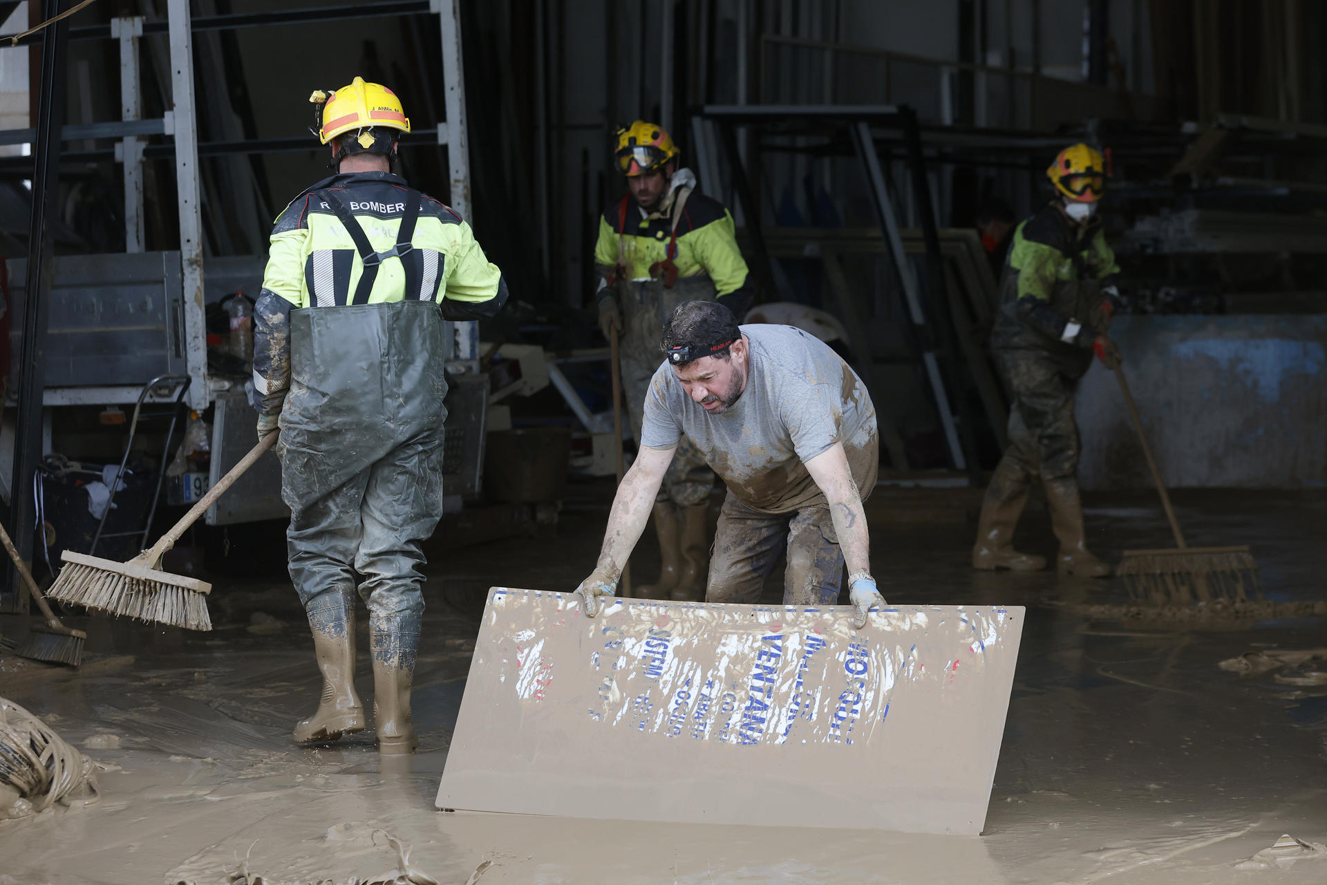 Un operario acompañado por un grupo de bomberos quitan lodo en una nave de Massanassa (Valencia), este miércoles. EFE/Miguel Ángel Polo
