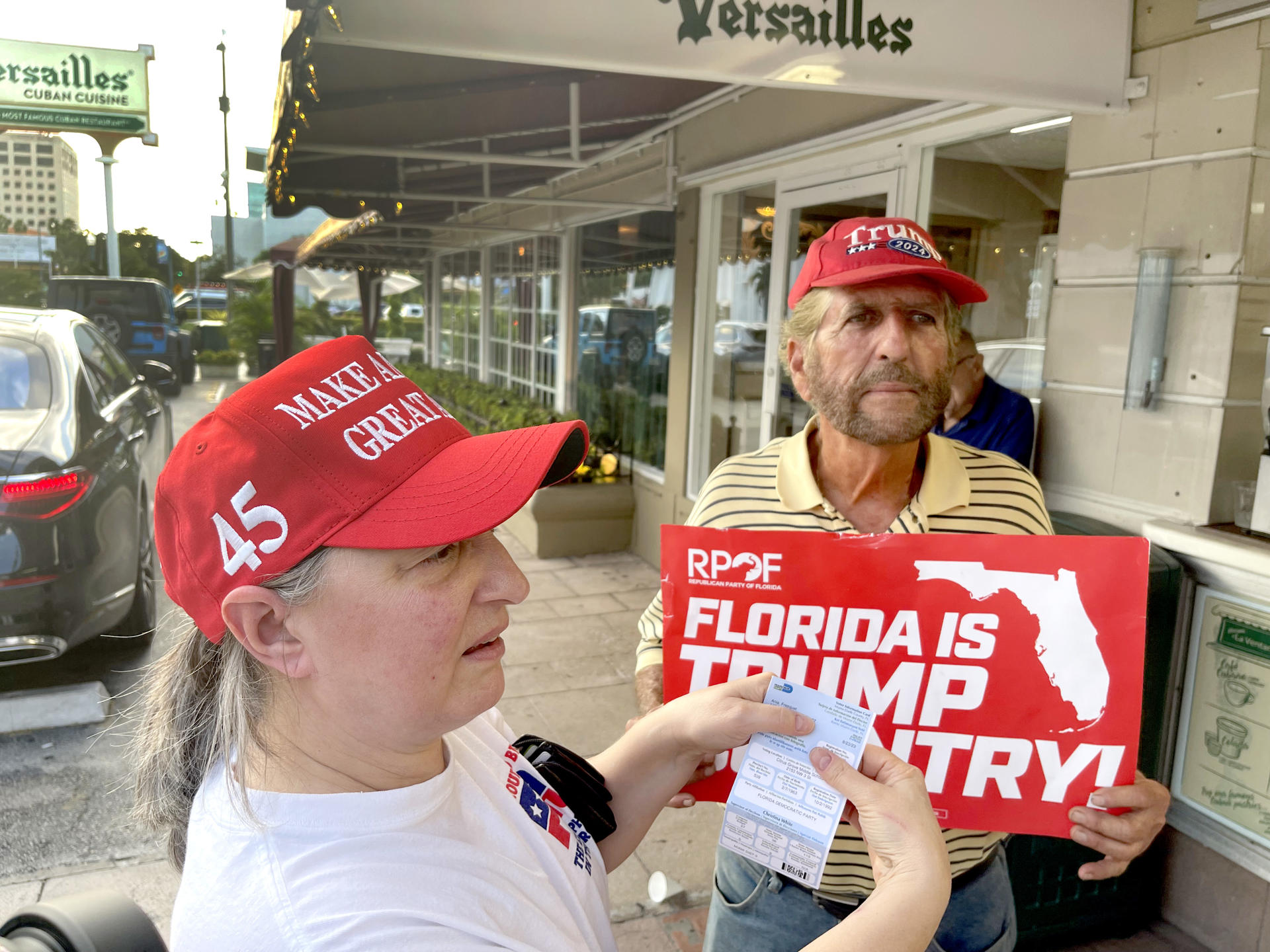 Ania Fresquet (i), una votante inscrita en la lista demócrata pero que vota por Donald Trump, muestra su tarjeta de votación junto a Miguel Saavedra, de la 'Vigilia Mambisa', el lunes 4 de noviembre de 2024 en frente del icónico restaurante Versailles de la Pequeña Habana en Miami, Florida (EE.UU.). EFE/Ana Milena Varón
