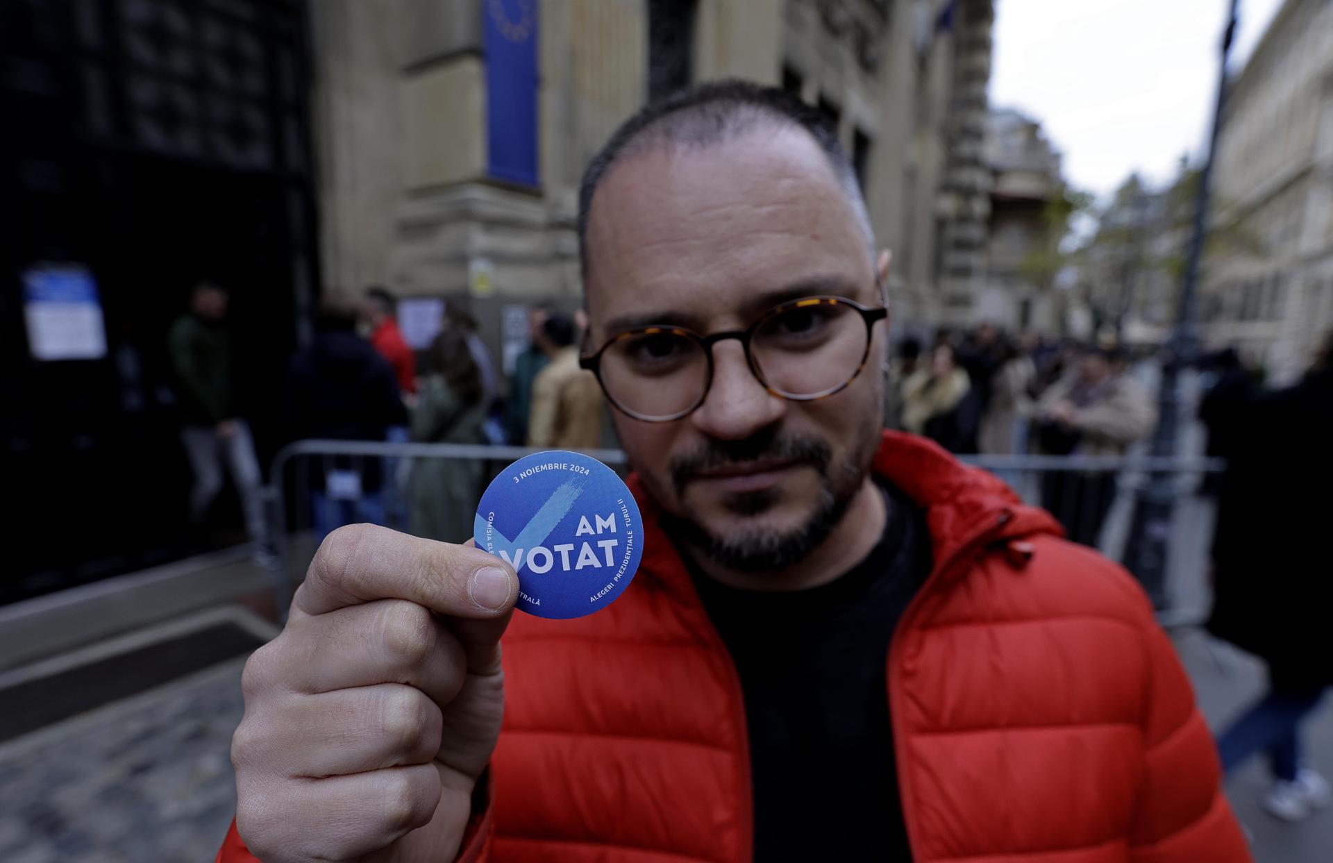 Un hombre moldavo residente en Rumania posa con una pegatina frente a un colegio electoral durante la segunda vuelta de las elecciones presidenciales moldavas, en el centro de Bucarest, Rumania, el 3 de noviembre de 2024.EFE/EPA/Robert Ghement
