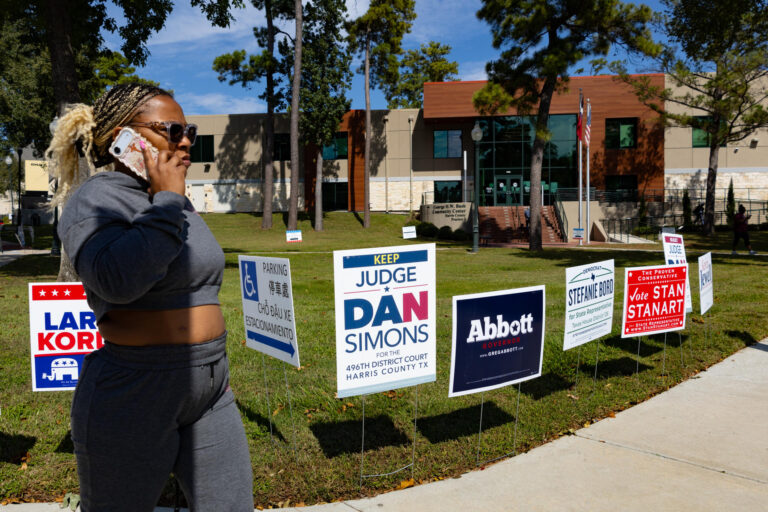 Fotografía del 19 de octubre de una mujer que camina junto a publicidad electoral durante la jornada de votación anticipada este lunes, en el centro George Bush en Houston, Texas (Estados Unidos). EFE/ Carlos Ramírez